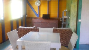 Un comedor con mobiliario de mimbre, un televisor pequeño sobre un mueble de madera y un ventilador en la pared.