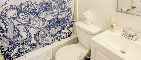 A bathroom with a white toilet, a sink with a mirror, and a shower curtain with a blue octopus design.