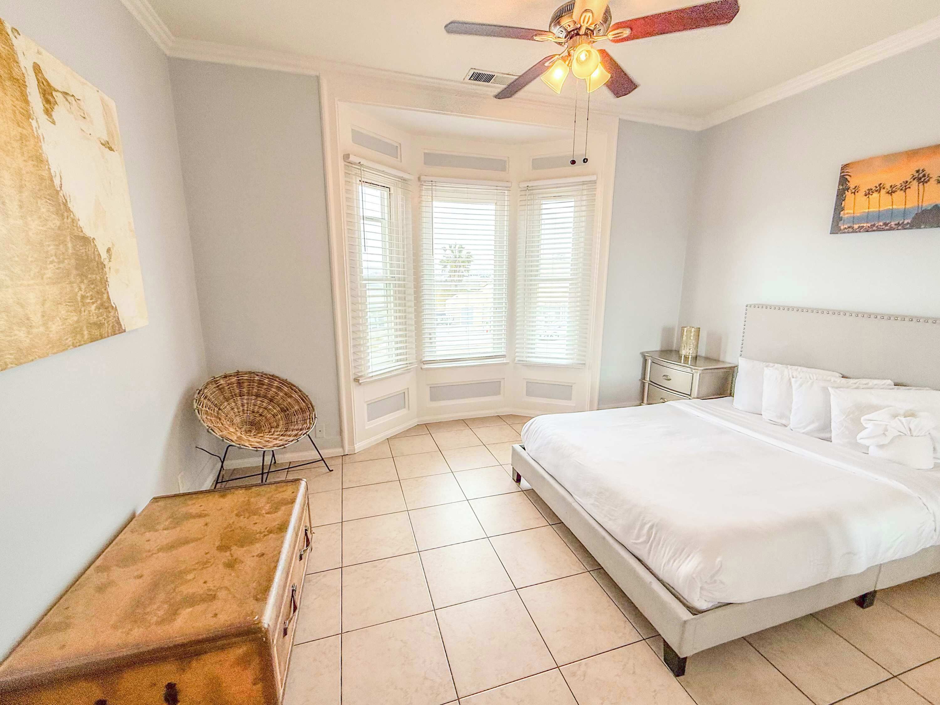 A bedroom with a large bed, a ceiling fan, and a window with blinds.