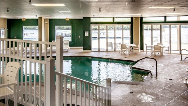 An indoor swimming pool with a tiled floor, a pool ladder, and a white fence. There are chairs and tables in the background, and a view of a body of water through large windows. - 6102 Towers. Luxury 6th Floor Towers, Beautifully Decorated. Free Wifi (Osage Beach)