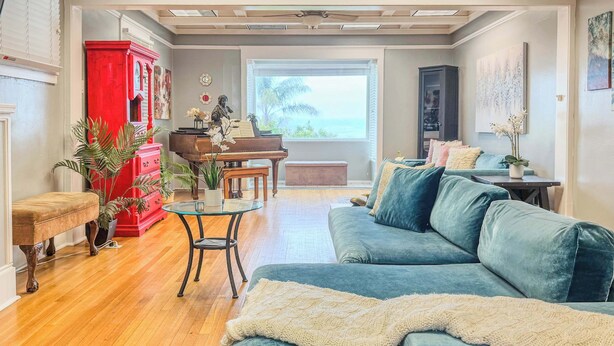 Sala de estar com piano, um armário vermelho, um sofá azul e vista para o mar.