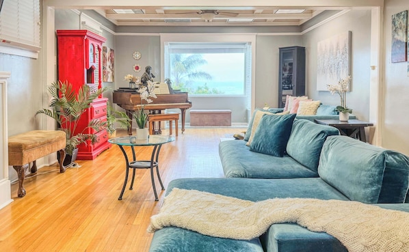 Ein Wohnzimmer mit Klavier, einem roten Schrank, einem blauen Sofa und Blick aufs Meer.