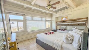 Quarto com cama, ventilador de teto, janela com persianas e vista externa.