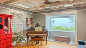 Um quarto com um piano, uma cômoda vermelha, um banco e vista para o exterior.