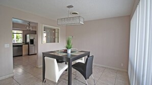 A modern kitchen with stainless steel appliances, a dining area with a table and chairs, and a hanging light fixture. - Exclusive Home By Traveline Plus (Hollywood)