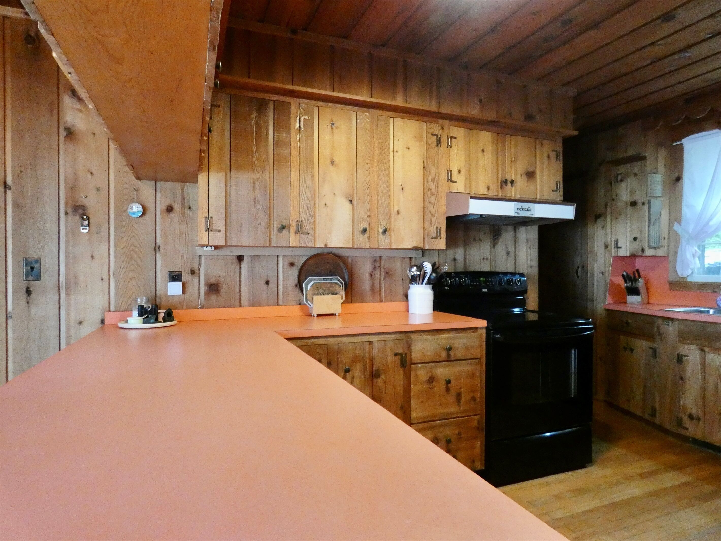 A wooden cabin-style kitchen with a large island, a stove, and wooden cabinets.