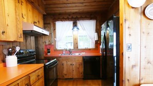 A compact kitchen with wooden cabinets, a stove, a sink, and a refrigerator. - Classic Lake Home (Alden)