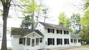 A white two-story house with a porch, a chimney, and a small garden area. - Classic Lake Home (Alden)