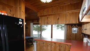 A wooden cabin kitchen with a black refrigerator, wooden cabinets, and a red countertop. - Classic Lake Home (Alden)