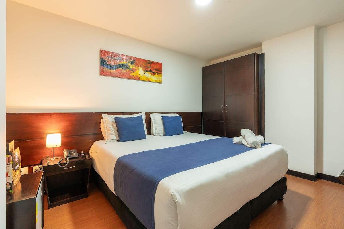 Ein Hotelzimmer mit einem großen Bett, einem Nachttisch mit Lampe, einem Telefon und einem Bild an der Wand.