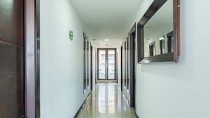 A long, narrow hallway with doors on both sides, leading to a bright room with a large window. - Hotel Bogota Resort (Bogotá)