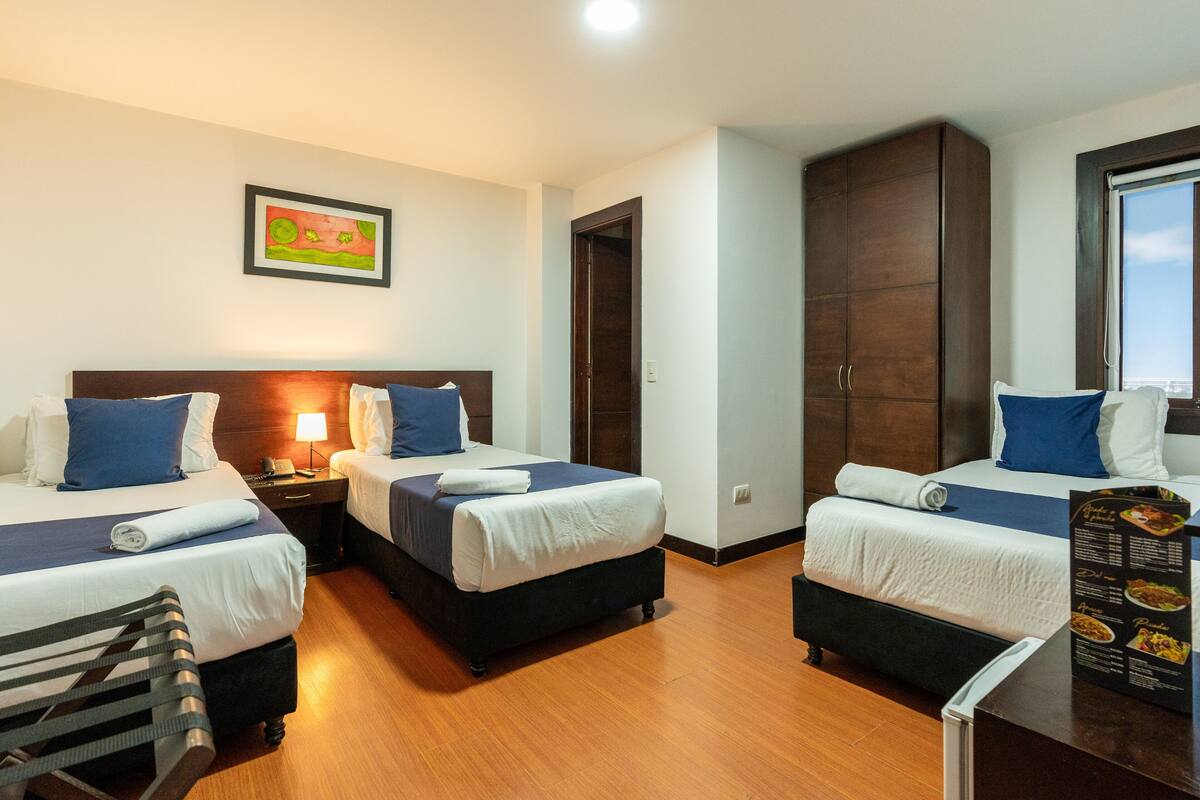 Ein Hotelzimmer mit zwei Betten, Holzboden, einem Gemälde an der Wand und einem Menüständer.