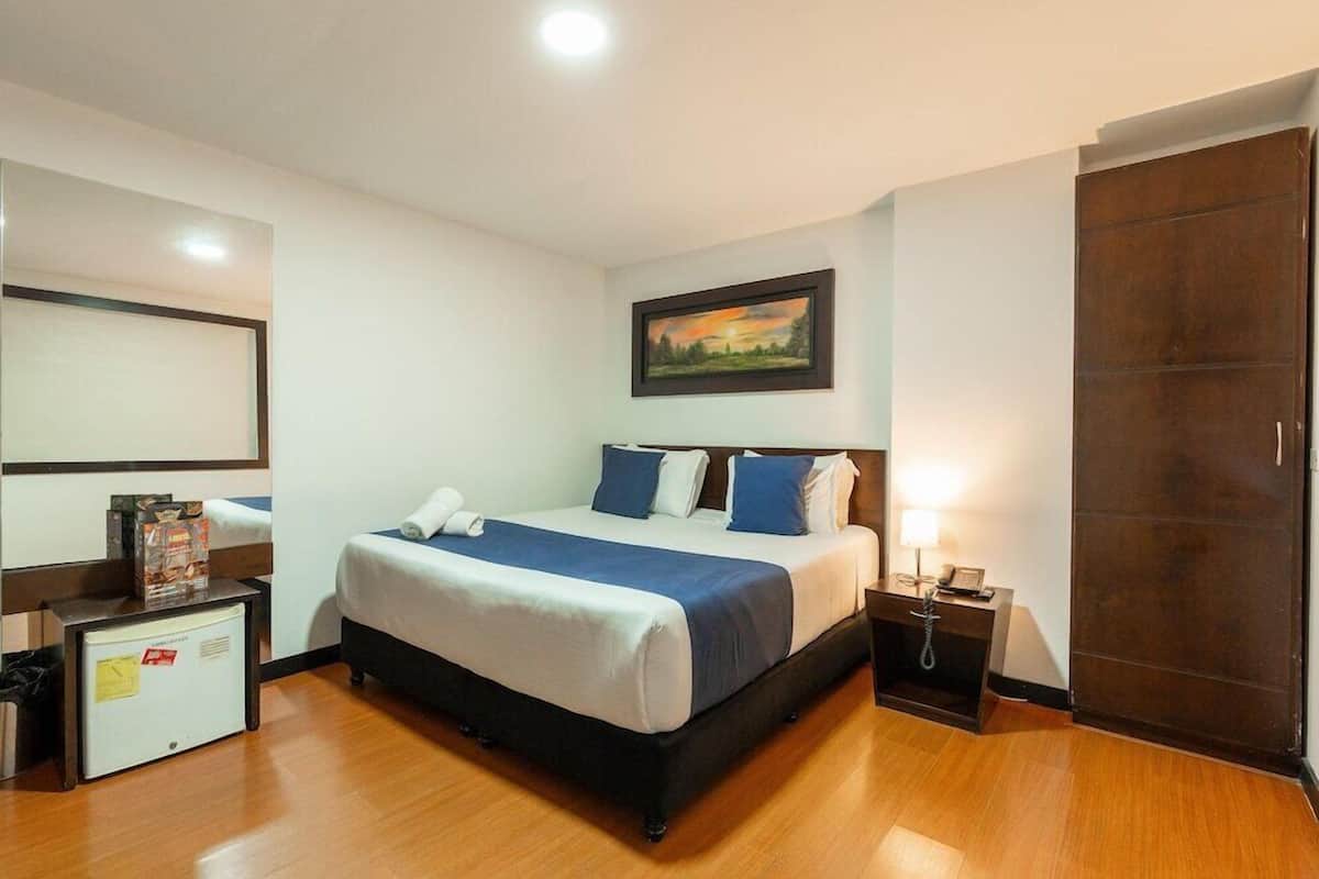 Ein Hotelzimmer mit einem großen Bett, einem Nachttisch, einem Schreibtisch, einer kleinen Kühlbox und einem Kleiderschrank.