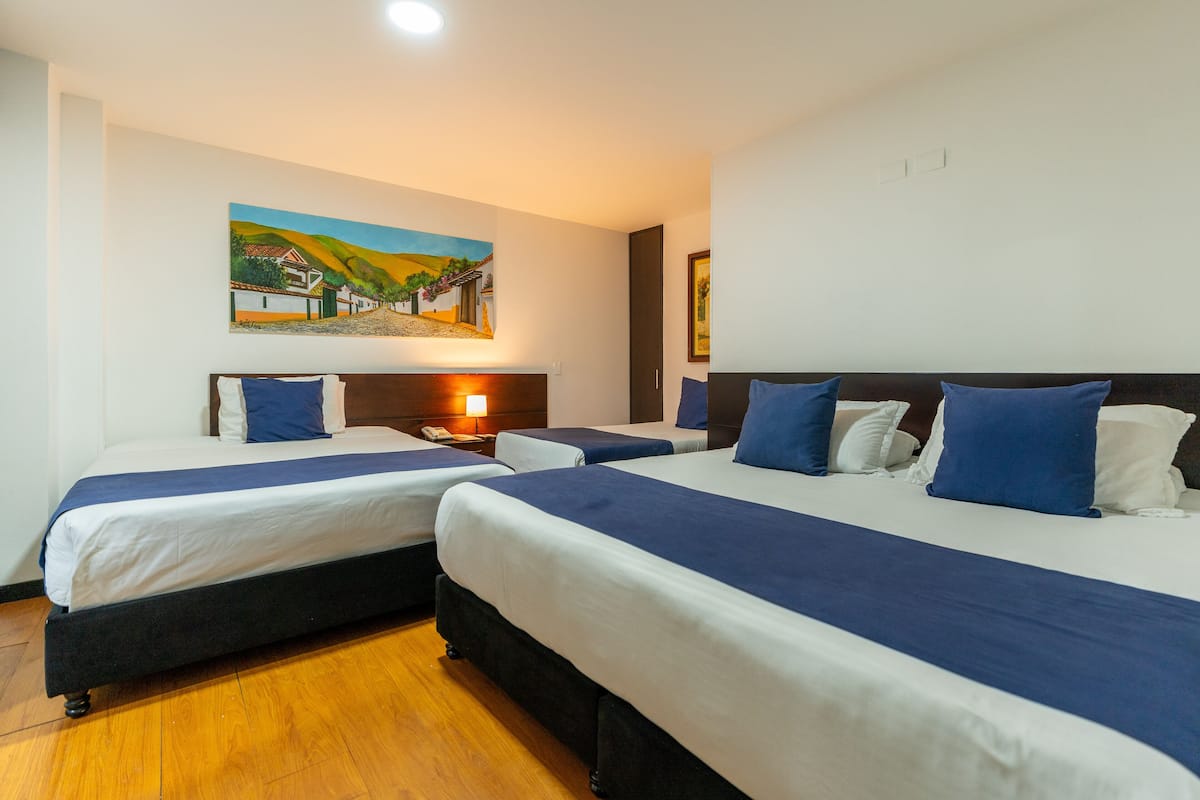 Ein Hotelzimmer mit zwei Betten, Holzboden, einem Gemälde an der Wand und einem Nachttisch mit Lampe.
