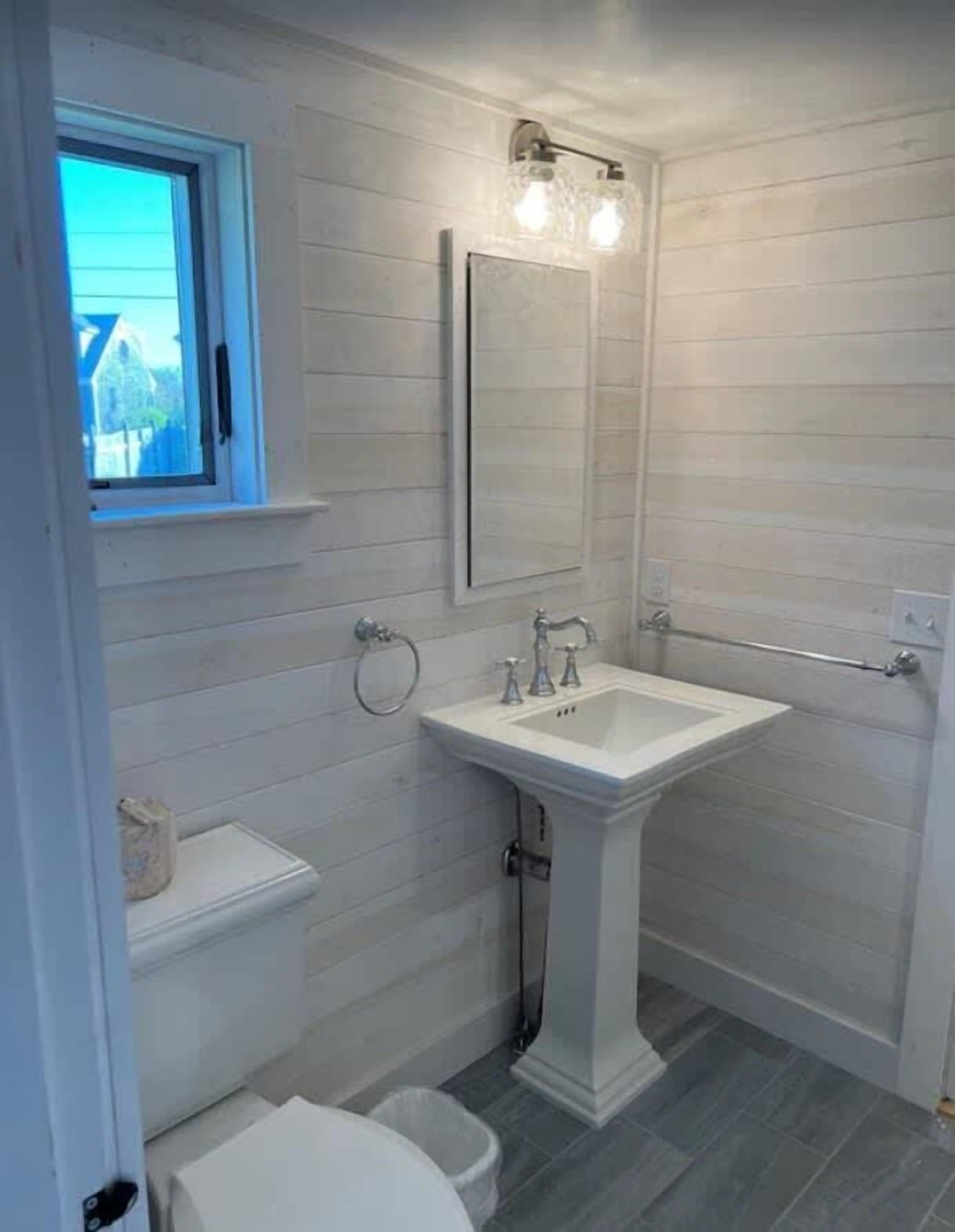 A bathroom with a pedestal sink, a window, and a towel rack.