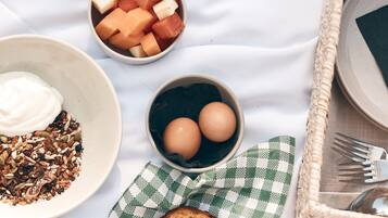 Ontbijt met toast, eieren, yoghurt, granola en meloen op een geruit kleed.