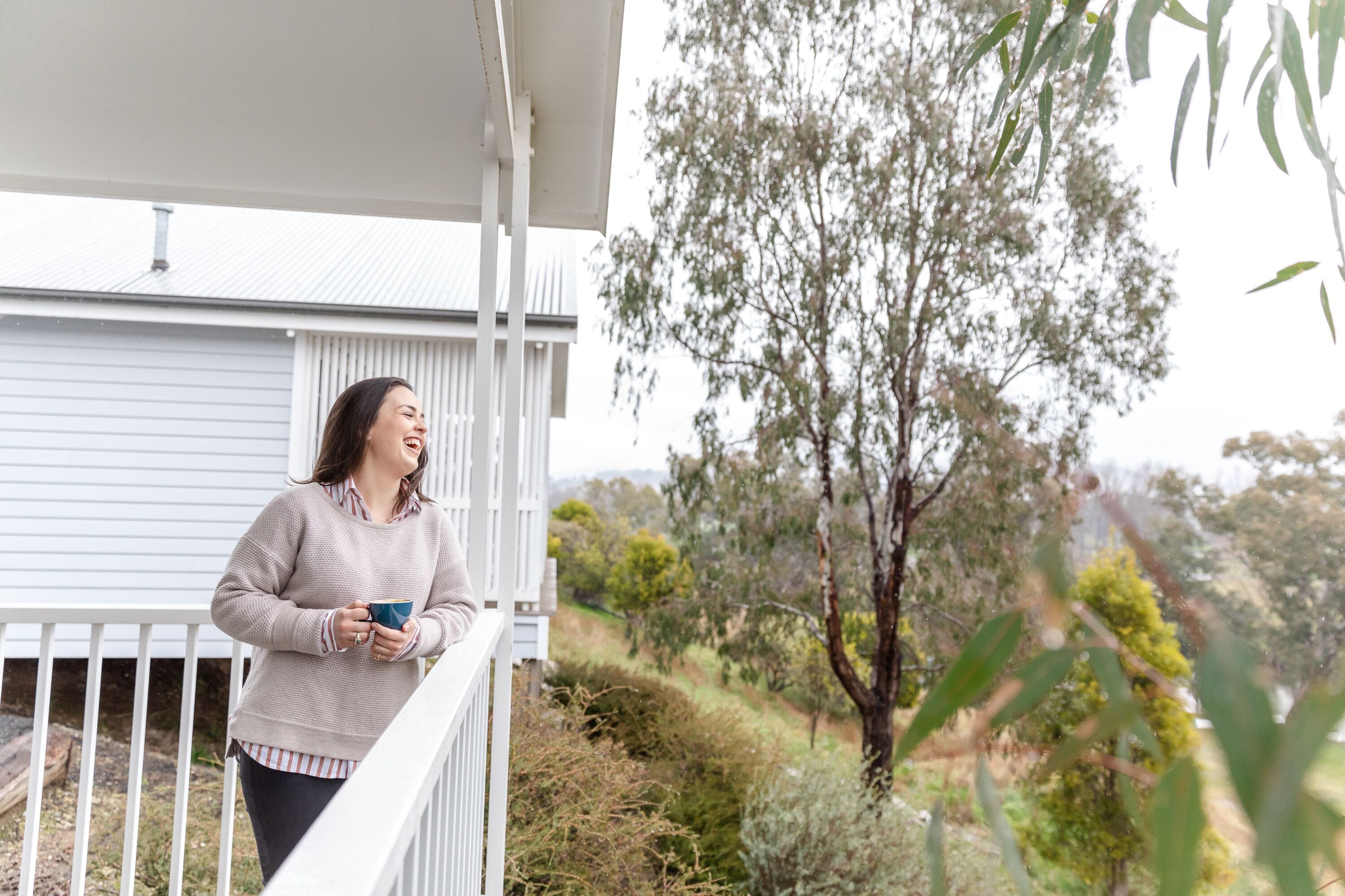 A person standing on a balcony with a view of a house and trees.