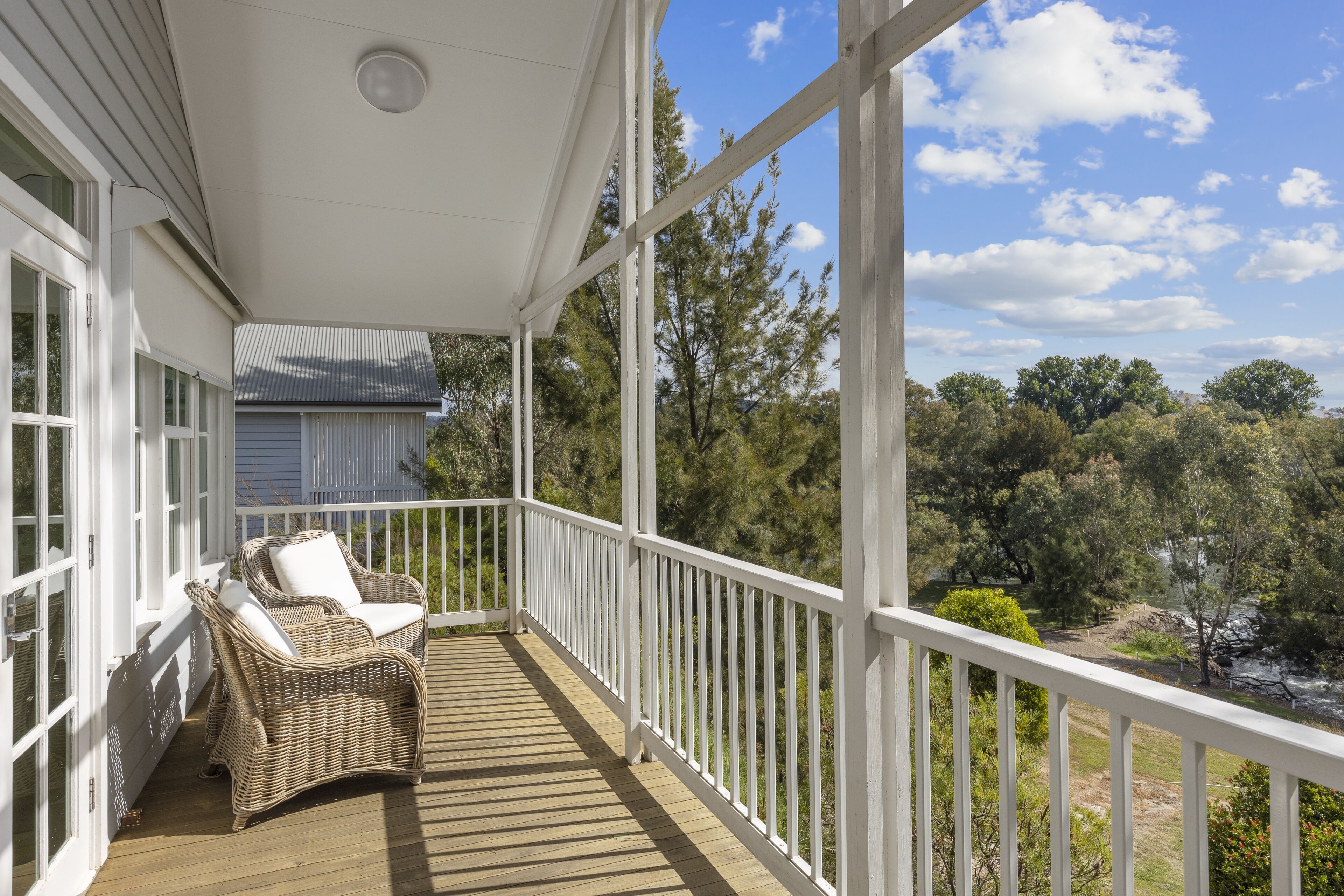 A wooden deck with wicker chairs, white railings, and a view of trees and a river.