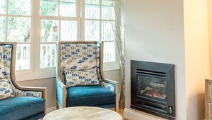 Una habitación con dos sillones tapizados en azul, una mesa redonda de madera, una chimenea y un par de cornamentas de ciervo montadas en la pared.