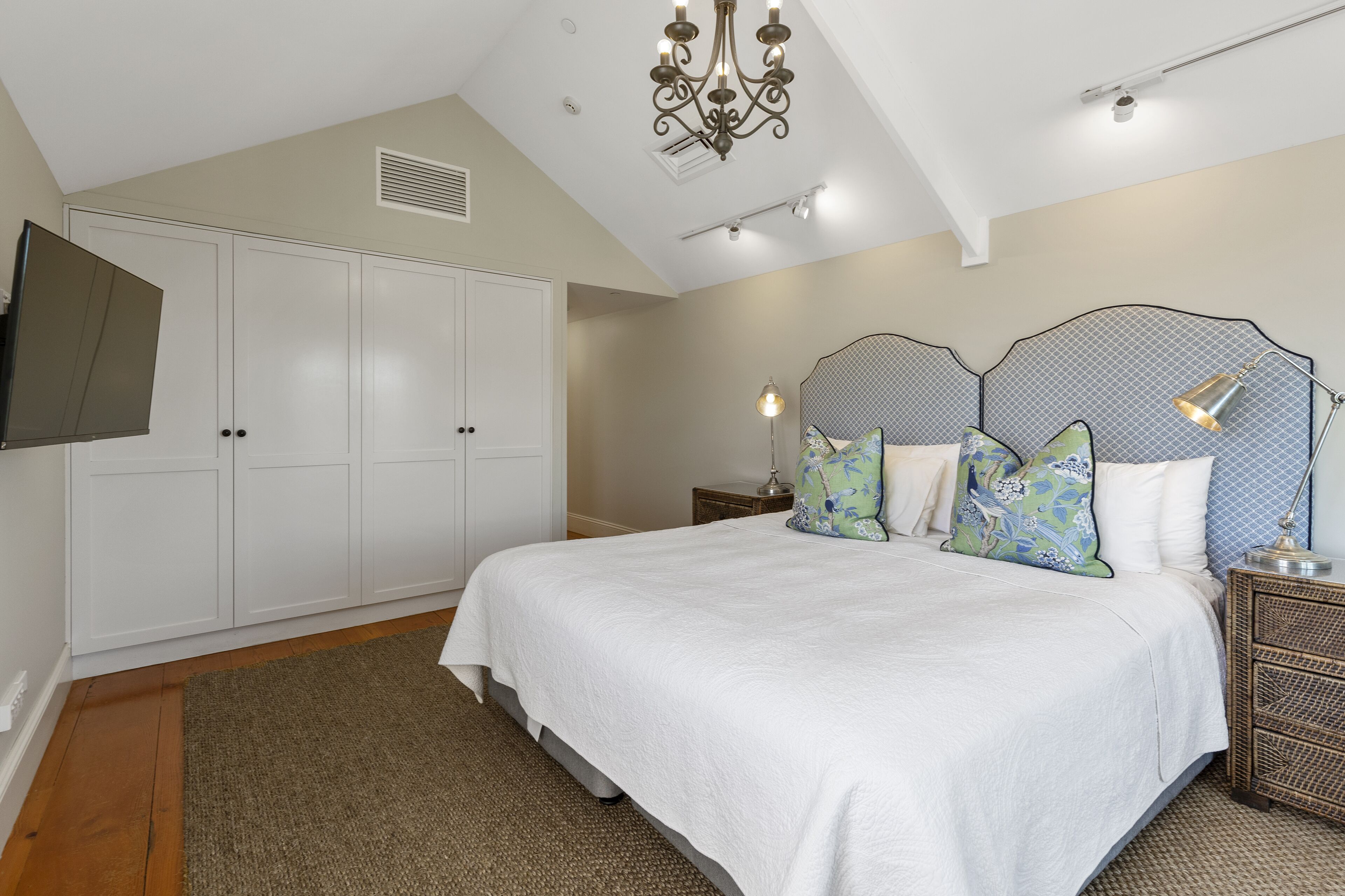 A bedroom with a large bed, white wardrobe, and a TV mounted on the wall.