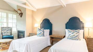 A hotel room with two beds, a wooden table, a chair, and a fireplace.