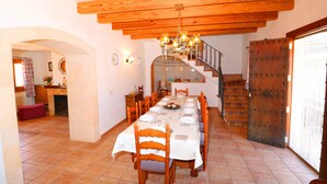 A dining area with a long table set for a meal, wooden chairs, a chandelier, and a staircase leading to an upper level. - Can Palea, Wi-fi free, private pool, garden, 15 minutes from the beach Es Trenc (Campos)