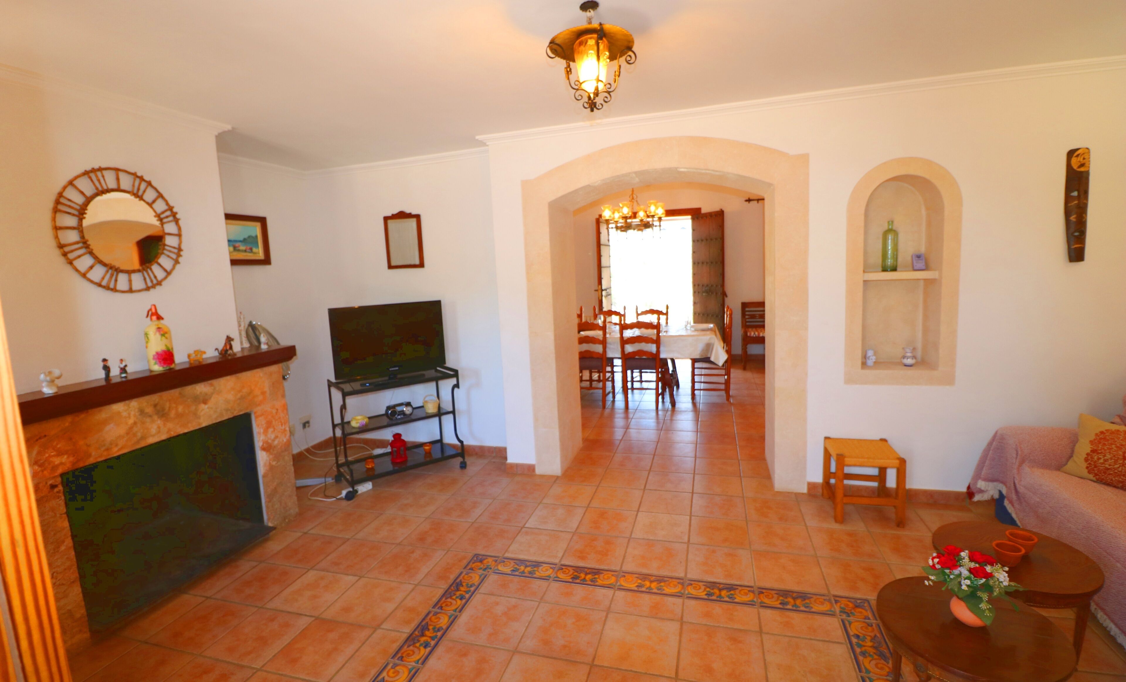 A living room with a fireplace, TV, dining area, and a hallway leading to another room.