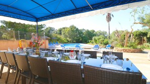 An outdoor dining area with tables and chairs under a blue canopy, overlooking a swimming pool and lush greenery. - Can Palea, Wi-fi free, private pool, garden, 15 minutes from the beach Es Trenc (Campos)