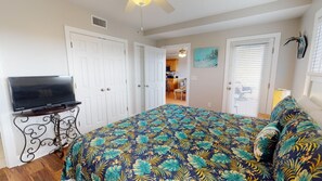 A bedroom with a bed, a TV on a stand, and a door leading to a kitchen. - Silver Shores 11 | Coastal Condo w/ Great Location (Tybee Island)