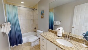 A bathroom with a bathtub, toilet, sink, and shower curtain. - Silver Shores 11 | Coastal Condo w/ Great Location (Tybee Island)