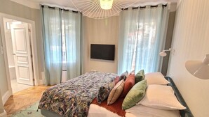 Ett sovrum med en säng, gardiner, en tv och en lampa.