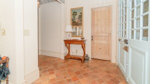 Un pasillo con una puerta de madera, una pared blanca con un cuadro enmarcado y una pequeña mesa con una lámpara.