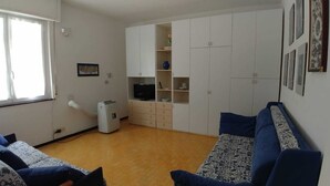 Un salón con un sofá azul, un televisor y un mueble blanco con estantes.
