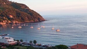 Un pueblo costero con barcos en el agua, edificios en la orilla y un paisaje montañoso de fondo.