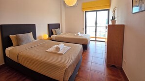 Hotellihuone, jossa on kaksi sänkyä, suuri ikkuna, puinen kaappi ja riippuvalaisin.
