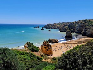 A coastal landscape with a sandy beach, rocky cliffs, and clear blue water.