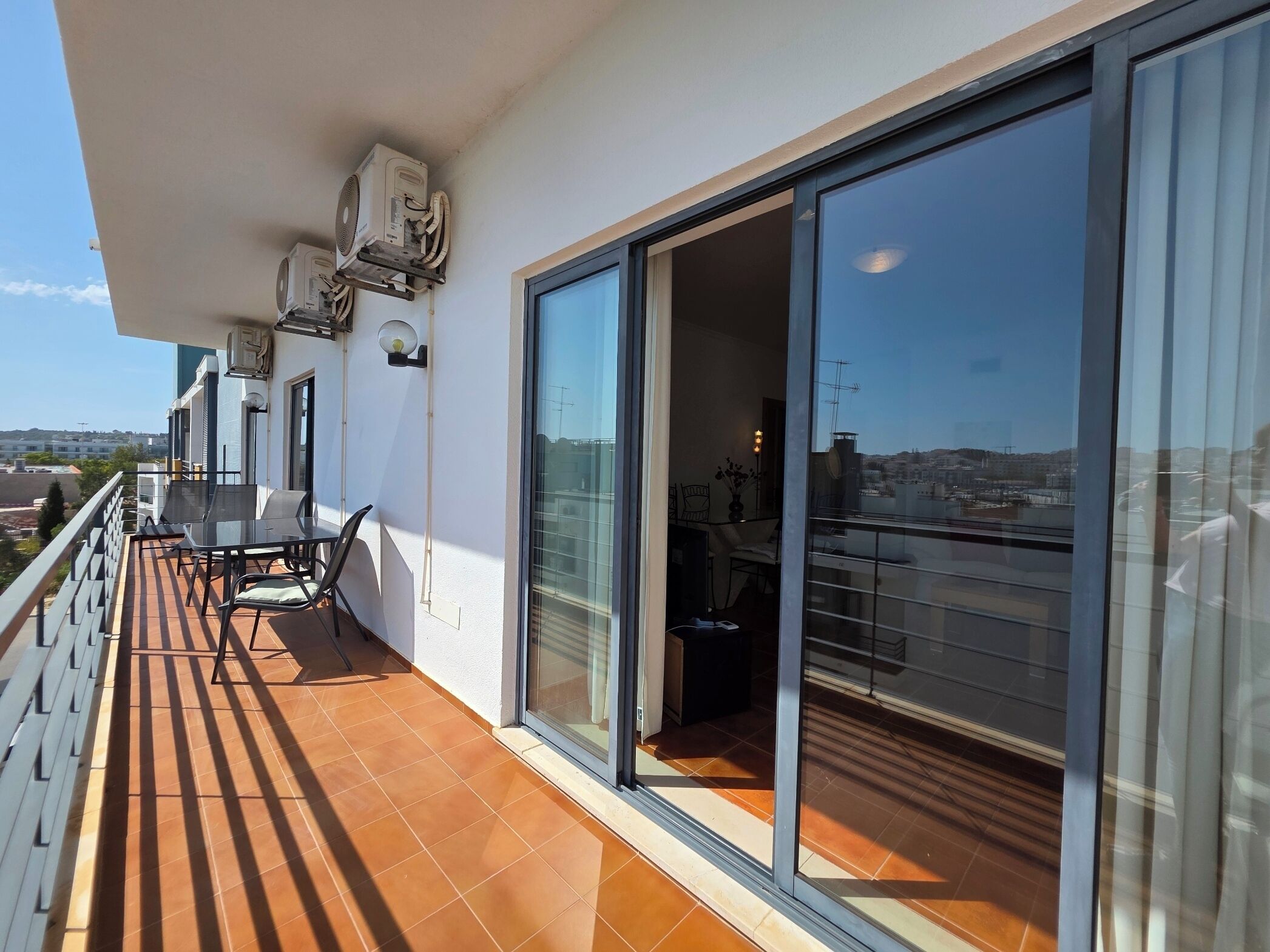 Ein Balkon mit Tisch und Stühlen, Klimaanlagen und einer Glastür zu einem Innenraum.