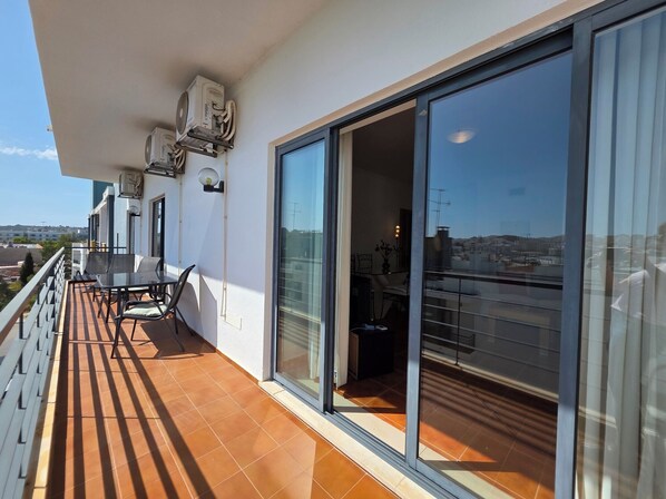 A balcony with a table and chairs, air conditioning units, and a sliding glass door leading to an interior space.