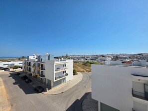 A modern multi-story building with a parking area, a marina in the background, and a clear sky.