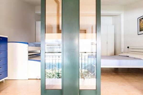 Una habitación con cama, escritorio y armario. Se ve follaje verde a través de la ventana.