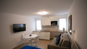 Ein gemütlicher Wohnbereich mit Küchenzeile, einer Essecke mit Tisch und Stühlen, einer Couch und einem an der Wand befestigten Fernseher.