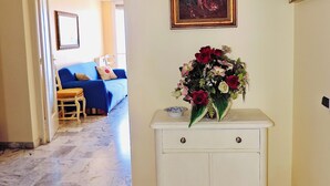En hall med ett vitt skåp, en tavla och en vas med blommor.