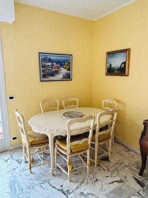 A dining area with a round table, six chairs, two wall-mounted paintings, and a door.