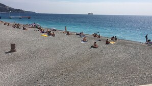 En strand med småsten där folk solar och badar.