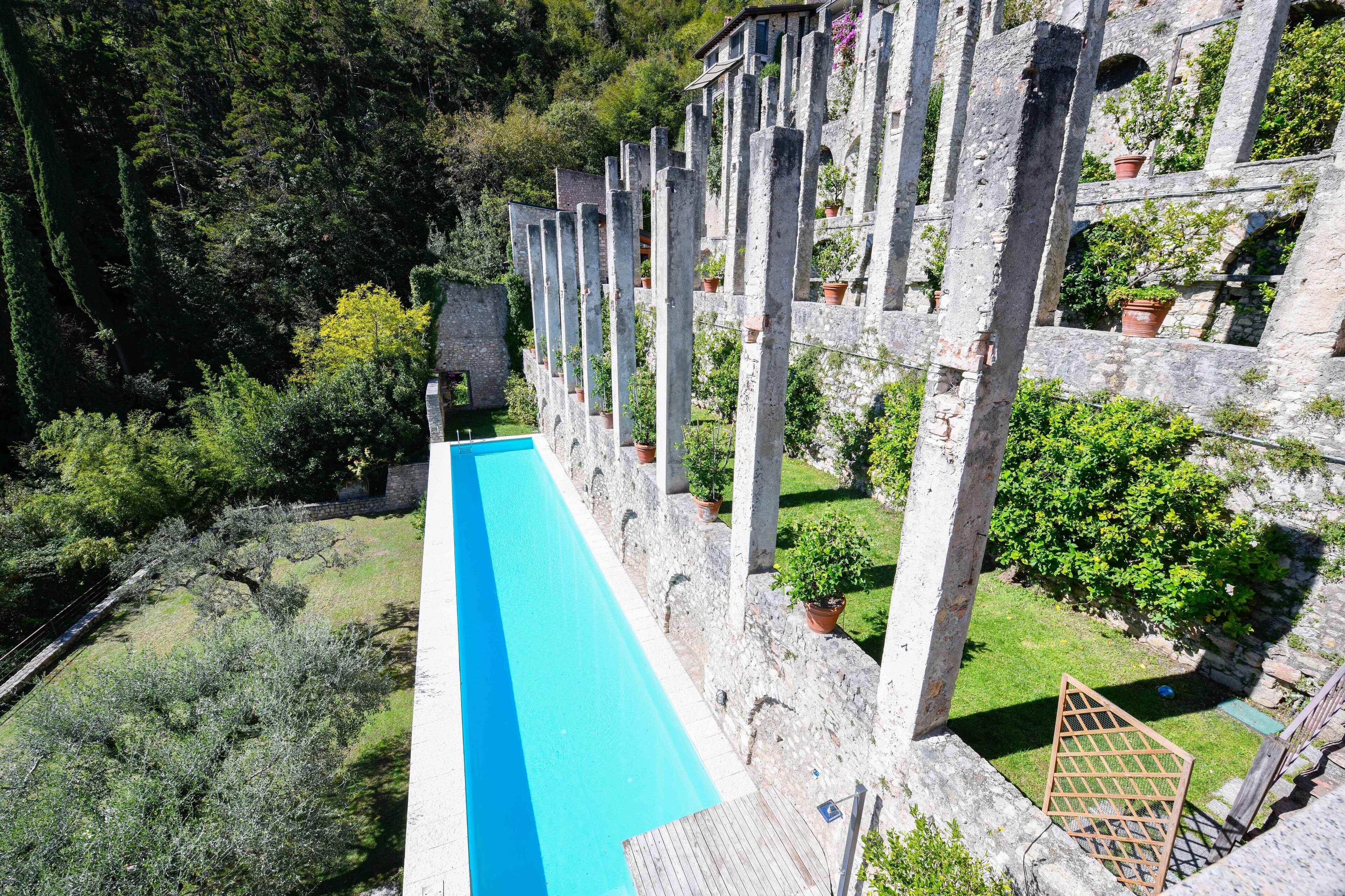 A long, narrow swimming pool with stone pillars and potted plants.