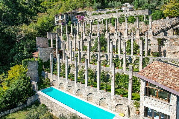 A stone building with a swimming pool, surrounded by lush greenery and terraced gardens.