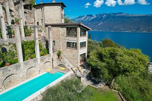Un edificio de piedra con piscina y mobiliario exterior, con vistas a un lago y montañas.