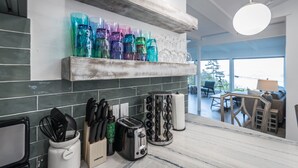 Une cuisine avec une étagère en bois où sont rangés des verres colorés, un grille-pain, une bouilloire et un bloc à couteaux.
