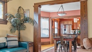 Una sala de estar con un sofá azul, una mesa de comedor con sillas, una planta grande y vigas de madera.
