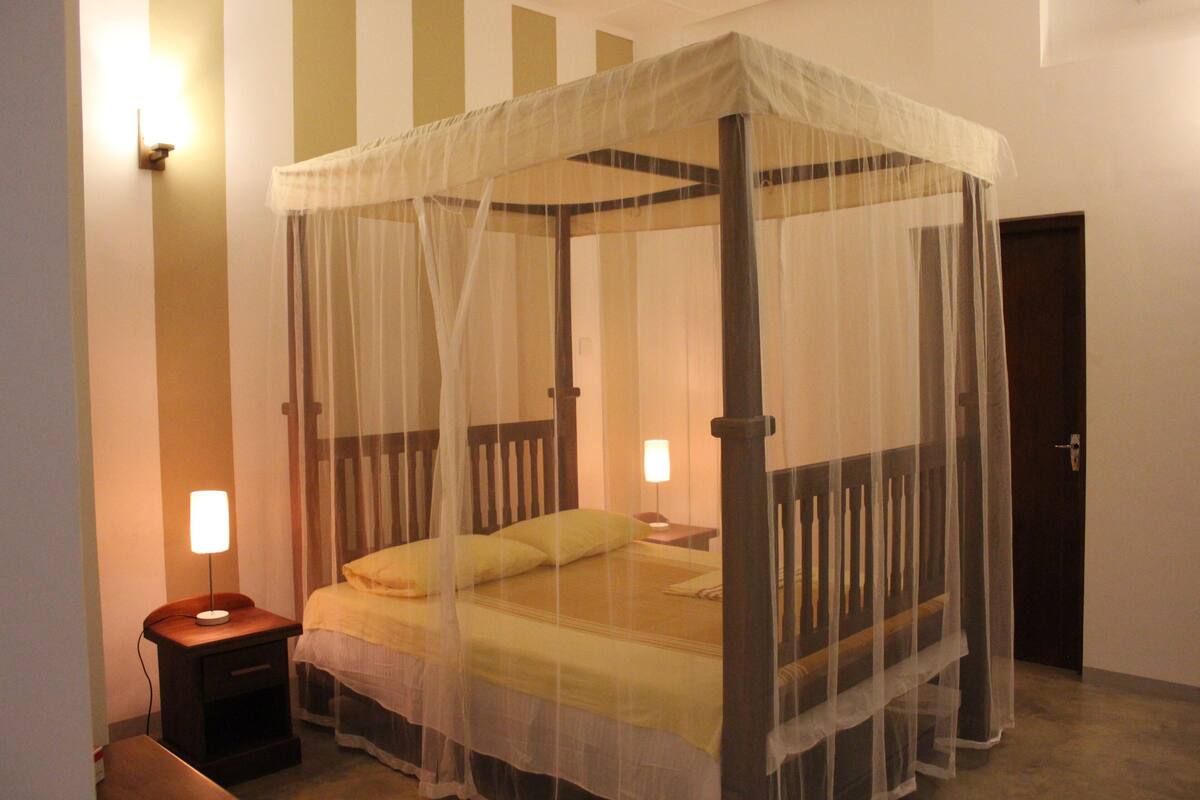 A four-poster bed with a canopy, bedside lamps, and a nightstand.
